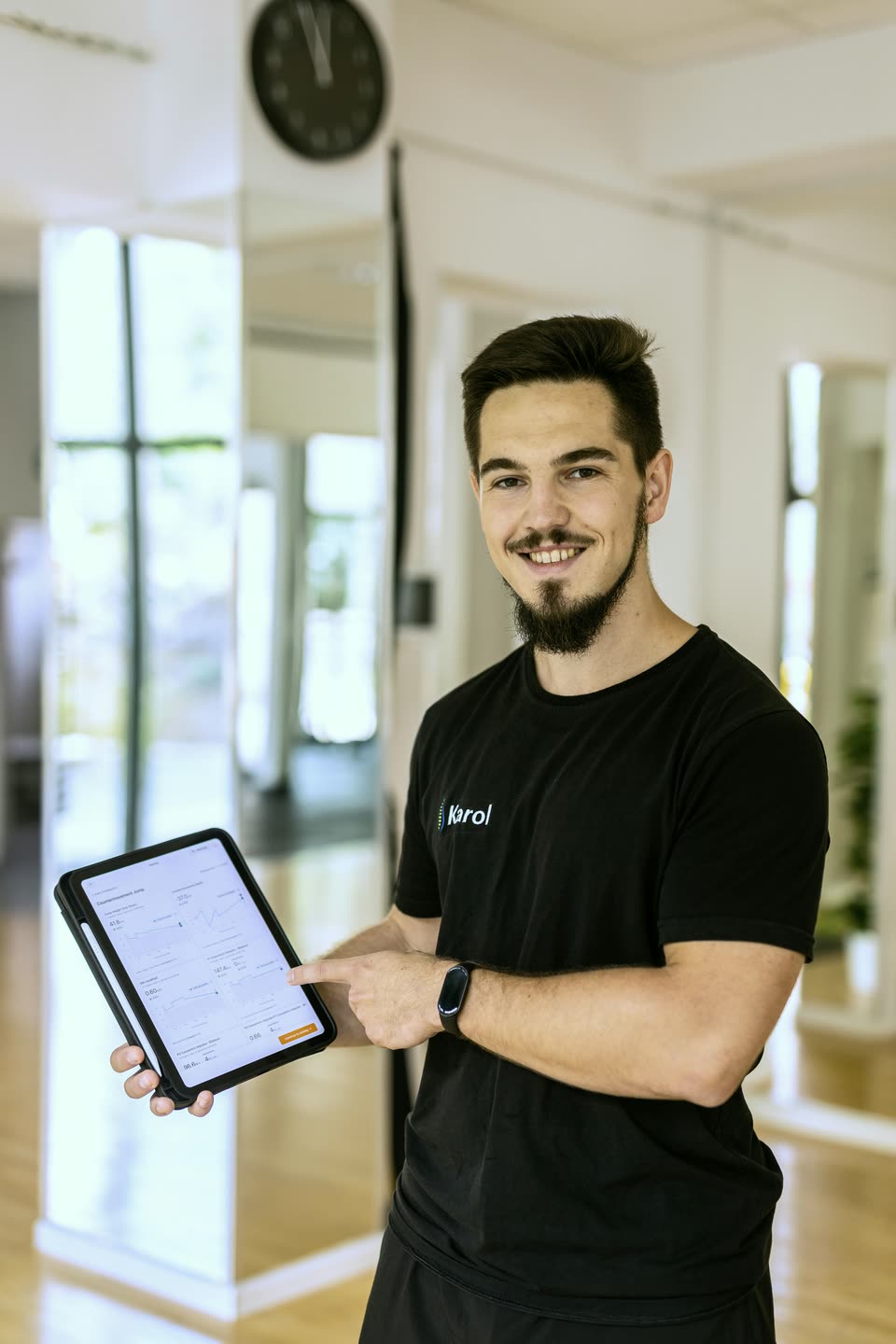 Karol Oniśkiewicz trzyma tablet z wykresami z testu skoku, wskazuje na ekran i patrzy w obiektyw